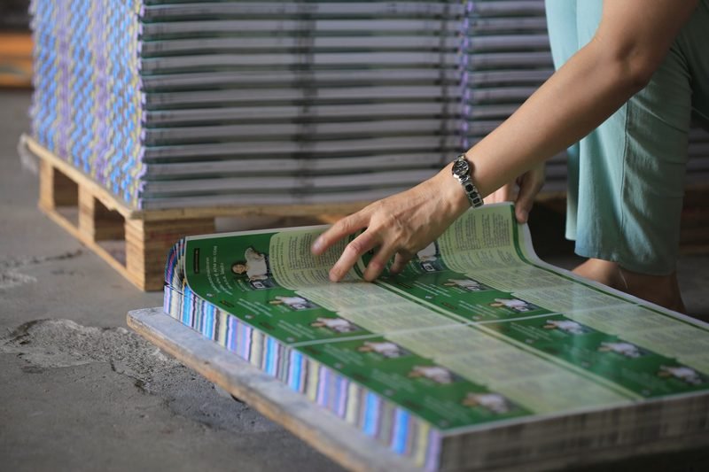Hands fanning a stack of freshly printed sheets on a pallet